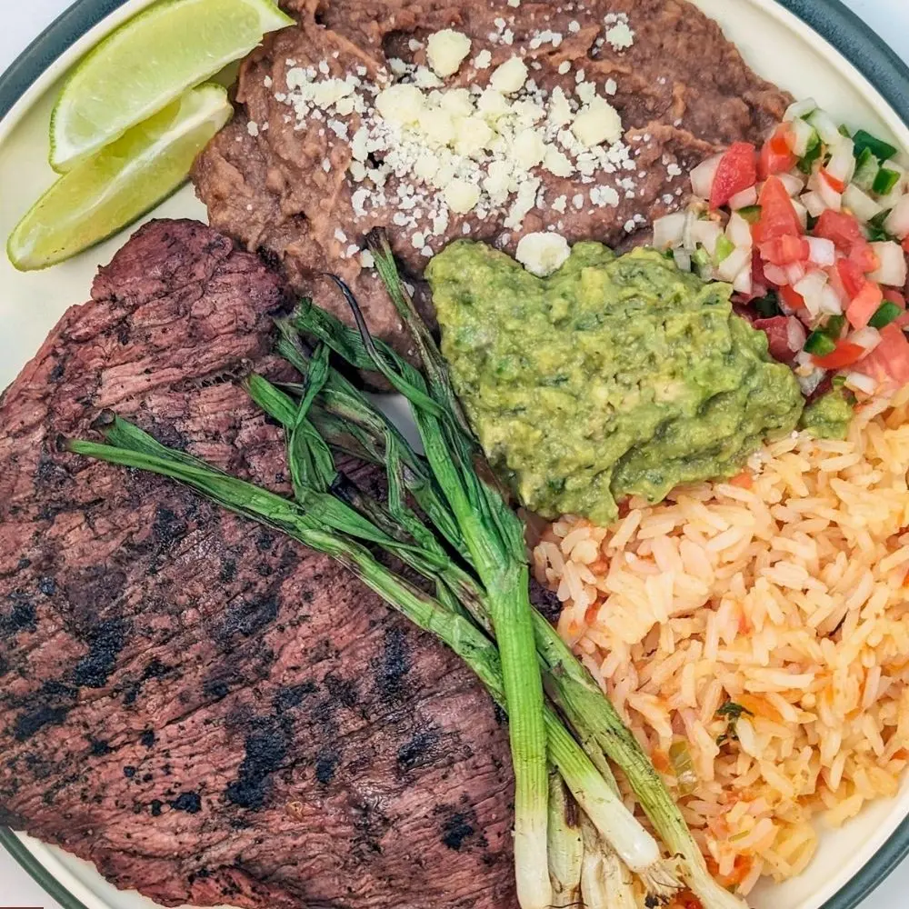 La Patrona carne asada plate with rice, beans, guacamole, and grilled onions
